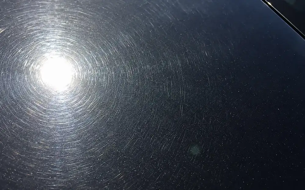 Fine swirl marks and wash scratches visible on dark car paint under bright light